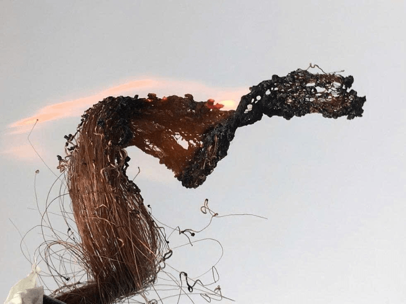A close-up of a hair strand being burned, showing melted, sticky residue and dark ash forming—commonly used to test whether the hair is real or synthetic.